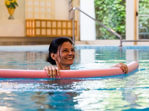 Hôtel thermal à Montegrotto : voyage de la santé Femme souriante dans une piscine intérieure avec une nouille de natation