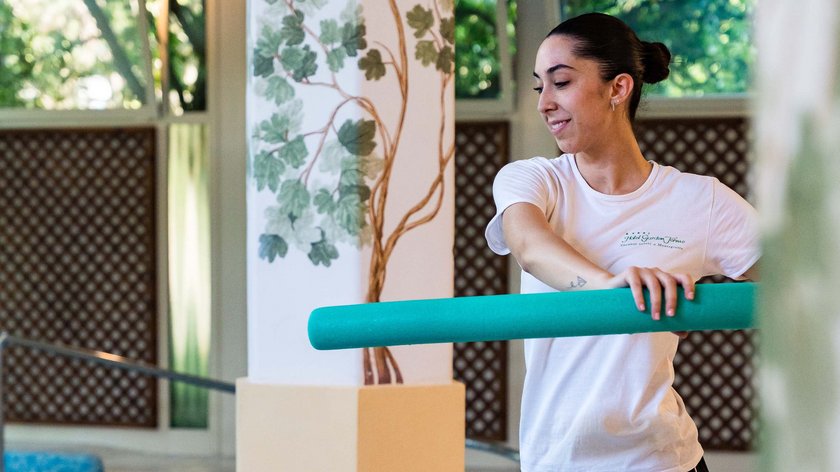 Rehabilitationszentrum Garden Terme Frau neben Schwimmbad mit blauem Schwimmnudel im Wassergymnastikraum