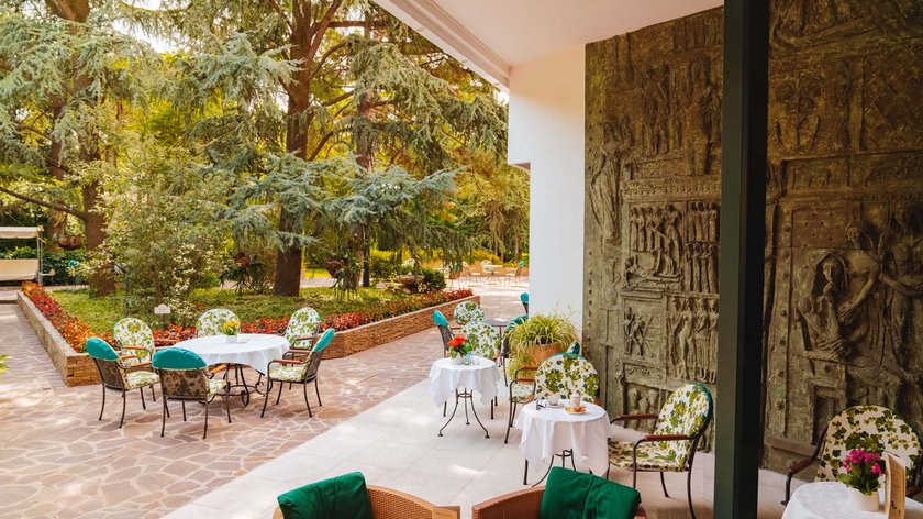 Hotel a Montegrotto Terme: sale e tesori d’arte Terrazza all'aperto con tavoli, sedie e vegetazione rigogliosa.